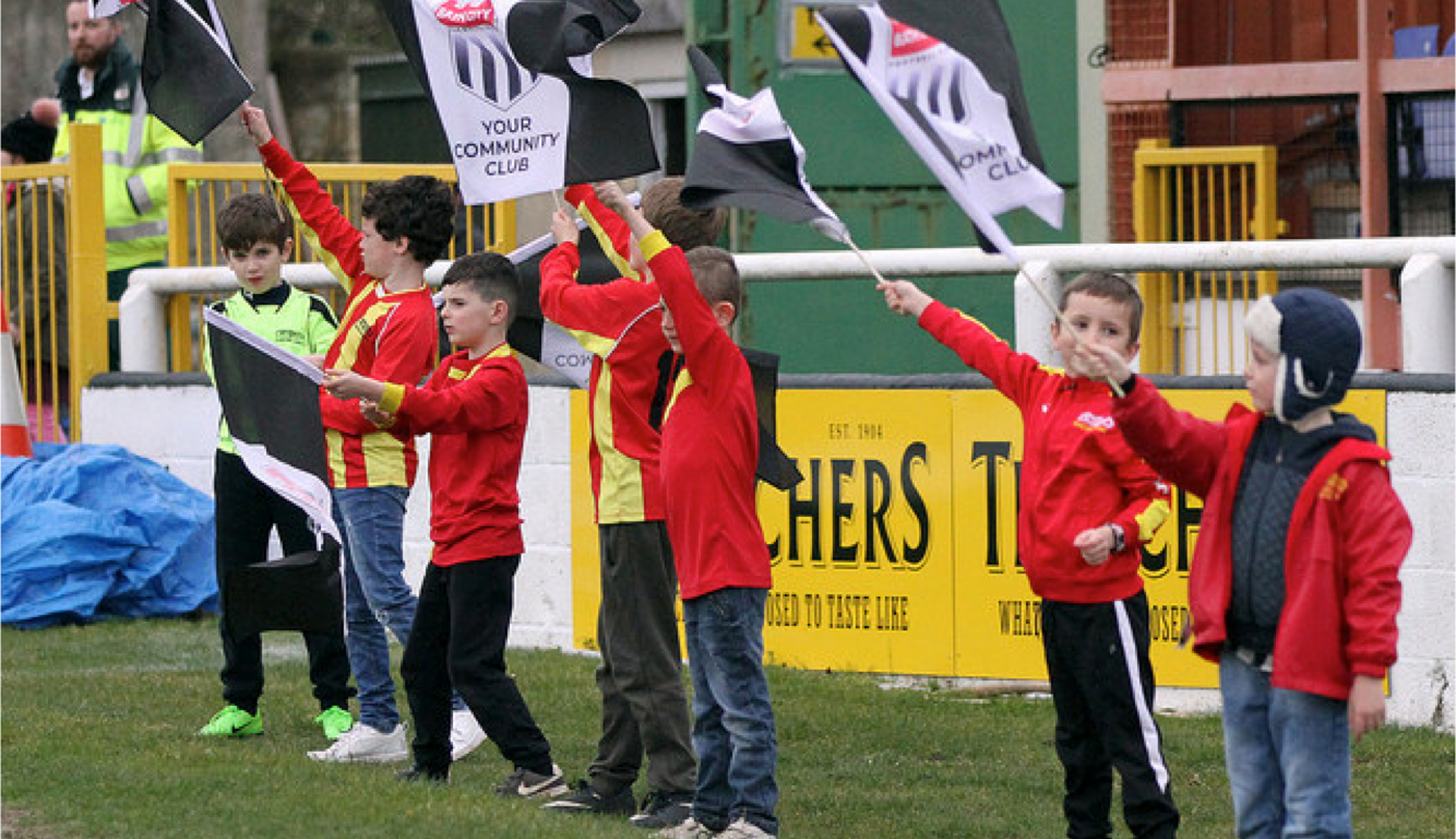 Kids wave flags on the sidelines of a Bath City football match